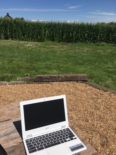 chromebook on picnic table next to cornfield