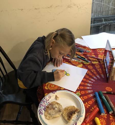 Emilia drawing while watching an instructional video, surrounded by art supplies and the remains of her breakfast